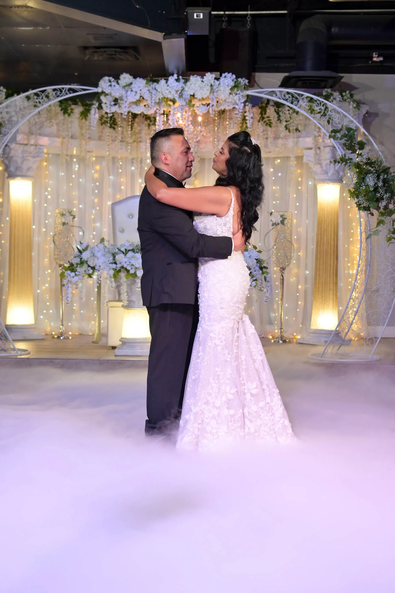 A couple sharing their first dance under a floral arch in the Moonlight Ballroom, with low fog across the floor