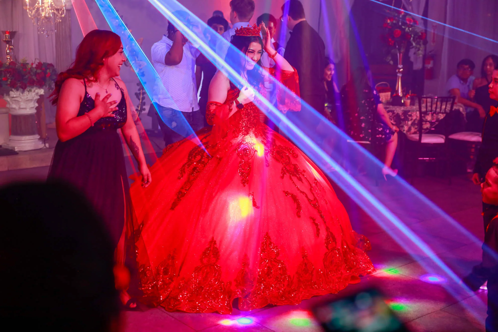 A quinceanera celebrant in a red ball gown on the dance floor as laser lighting sweeps the Moonlight Ballroom