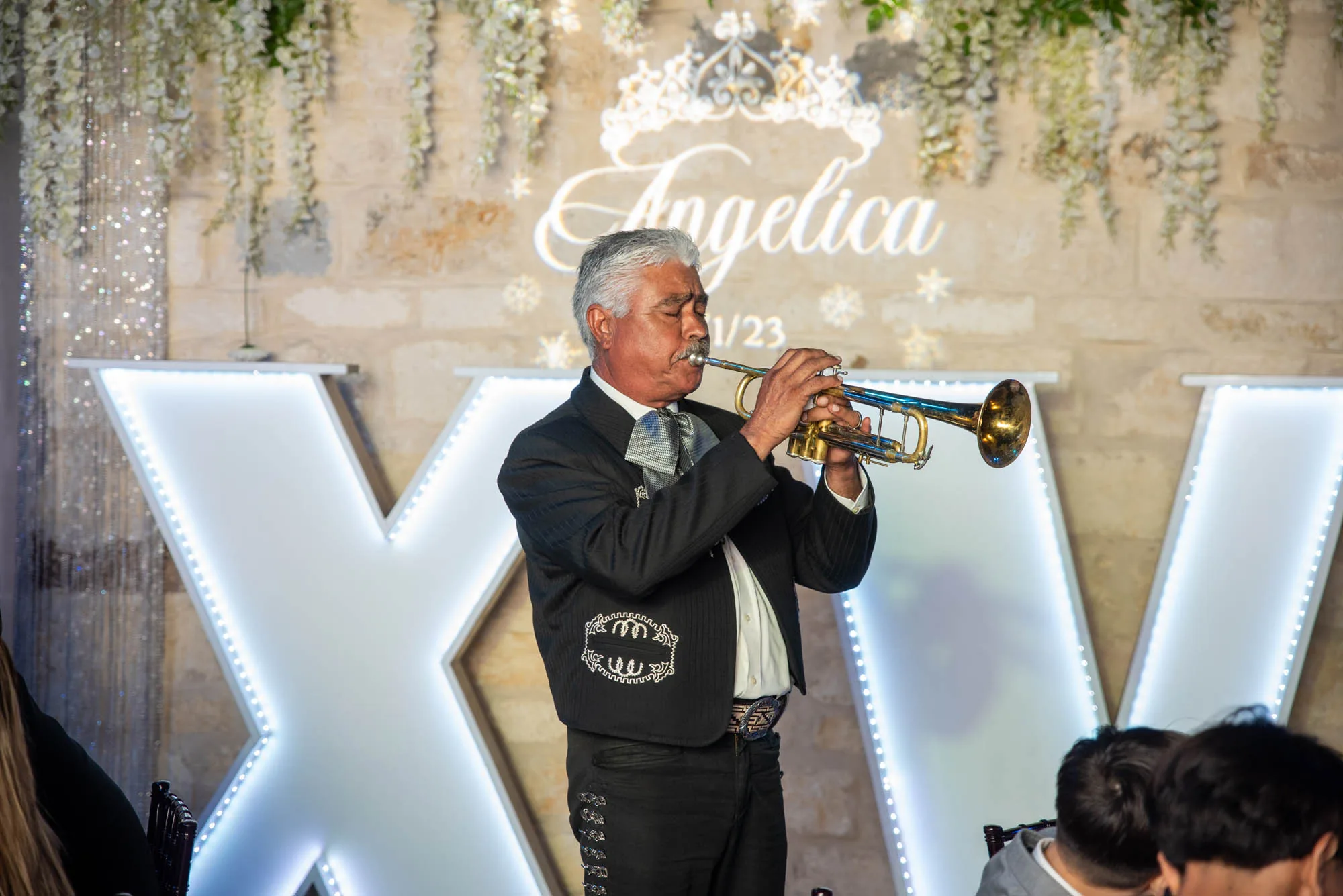 A mariachi trumpeter performing beside lit XV letters at a quinceanera in the Moonlight Ballroom