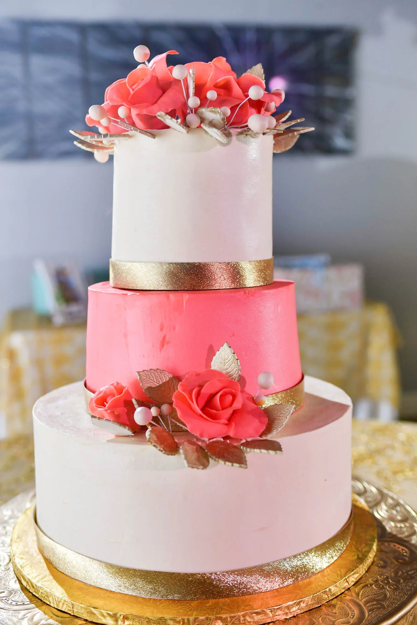 A three-tier coral and white celebration cake with sugar roses on a gold cake board