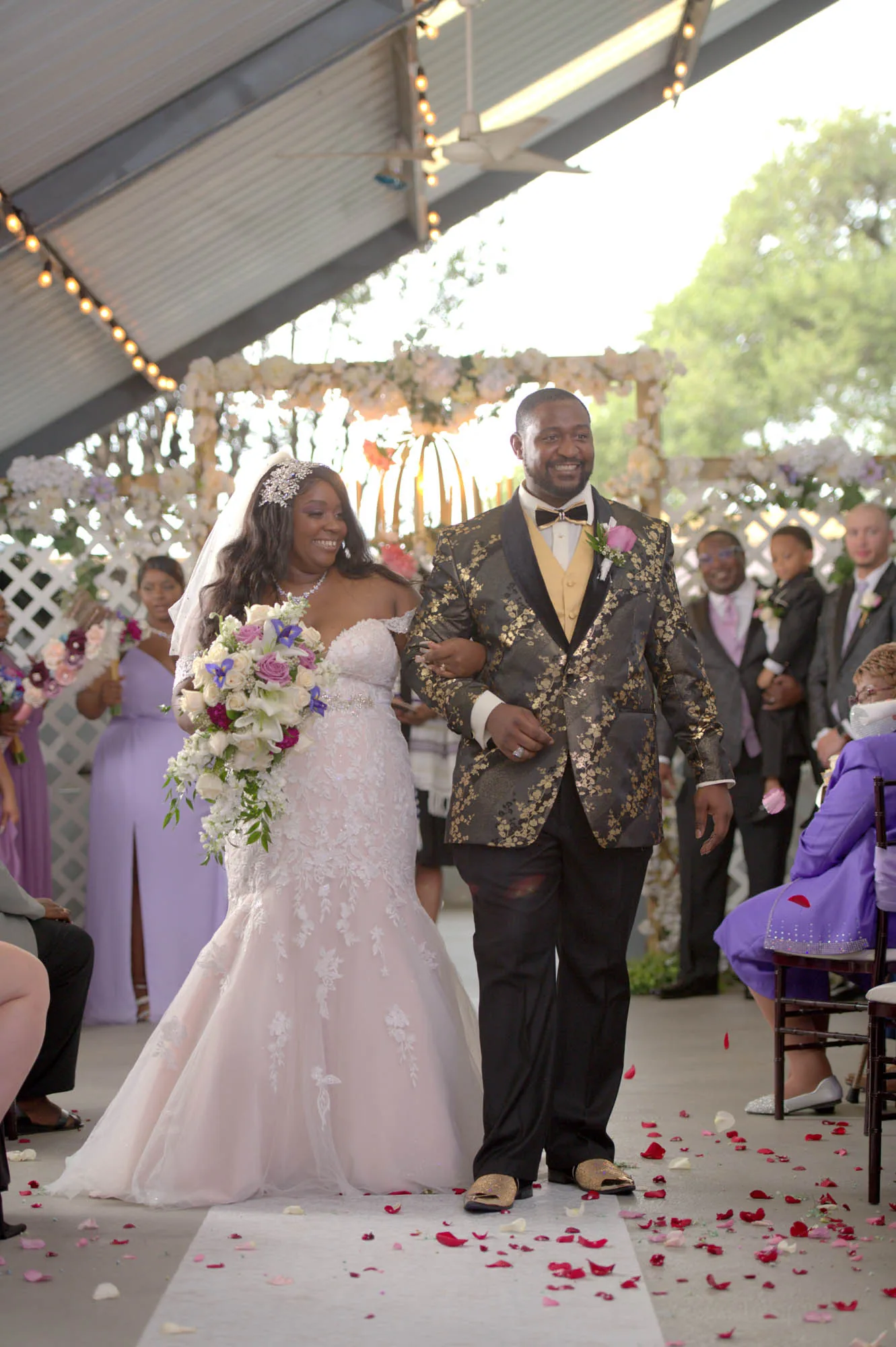 A bride and groom walking the aisle together after their ceremony, with rose petals on the floor